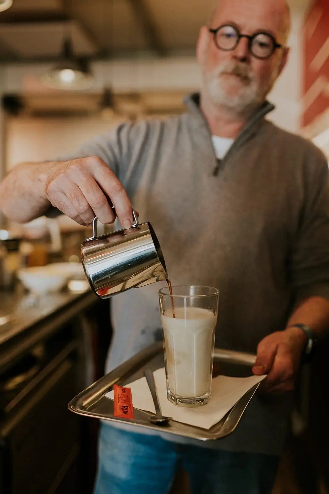 Barman werkt een koffie af op een dienblad met ROM-suikerzakjes