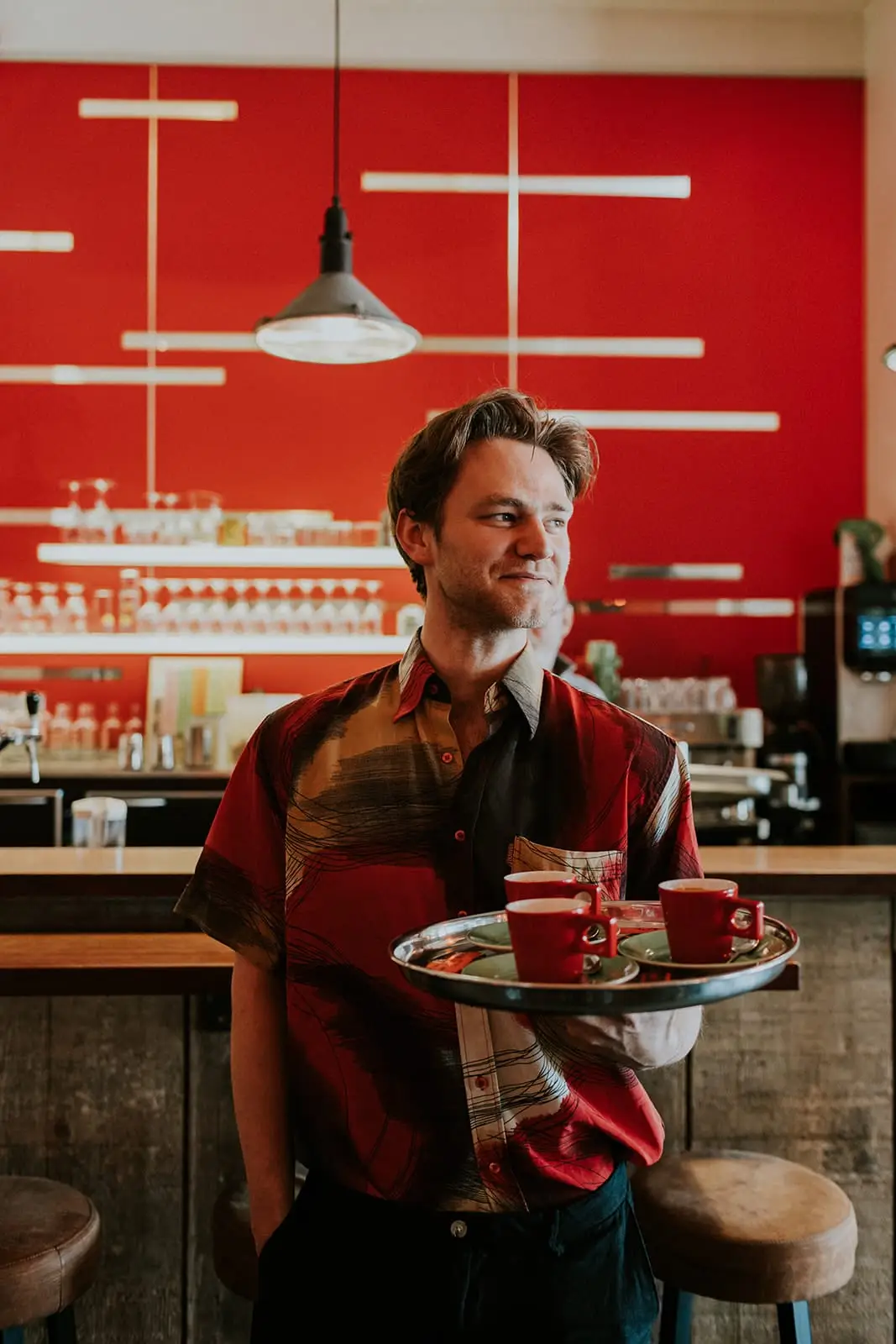 Glimlachende ober met een dienblad rode ROM-espressokopjes voor de rode bar