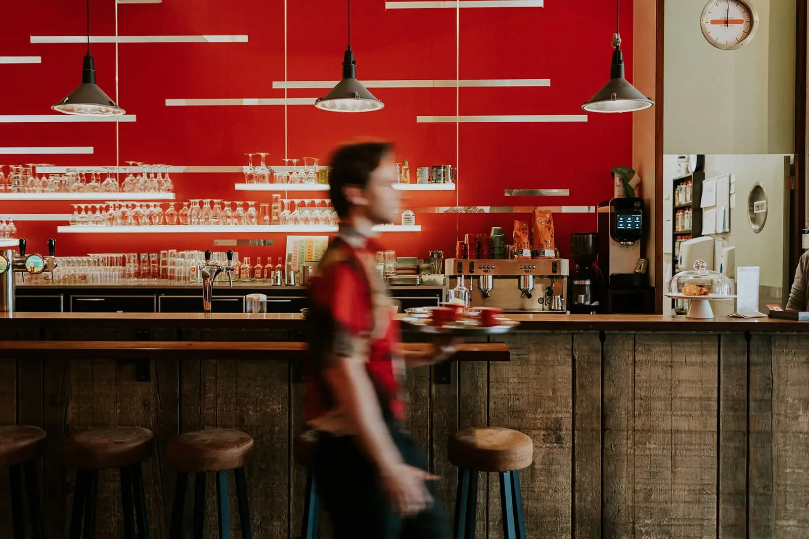 Ober met dienblad passeert de rode bar van een koffiebar