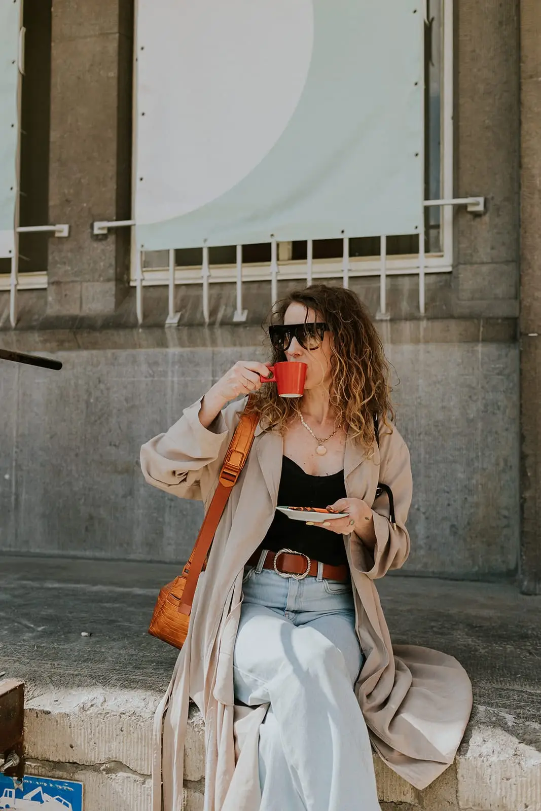 Gast drinkt espresso uit een rood ROM-kopje op een zonnig terras