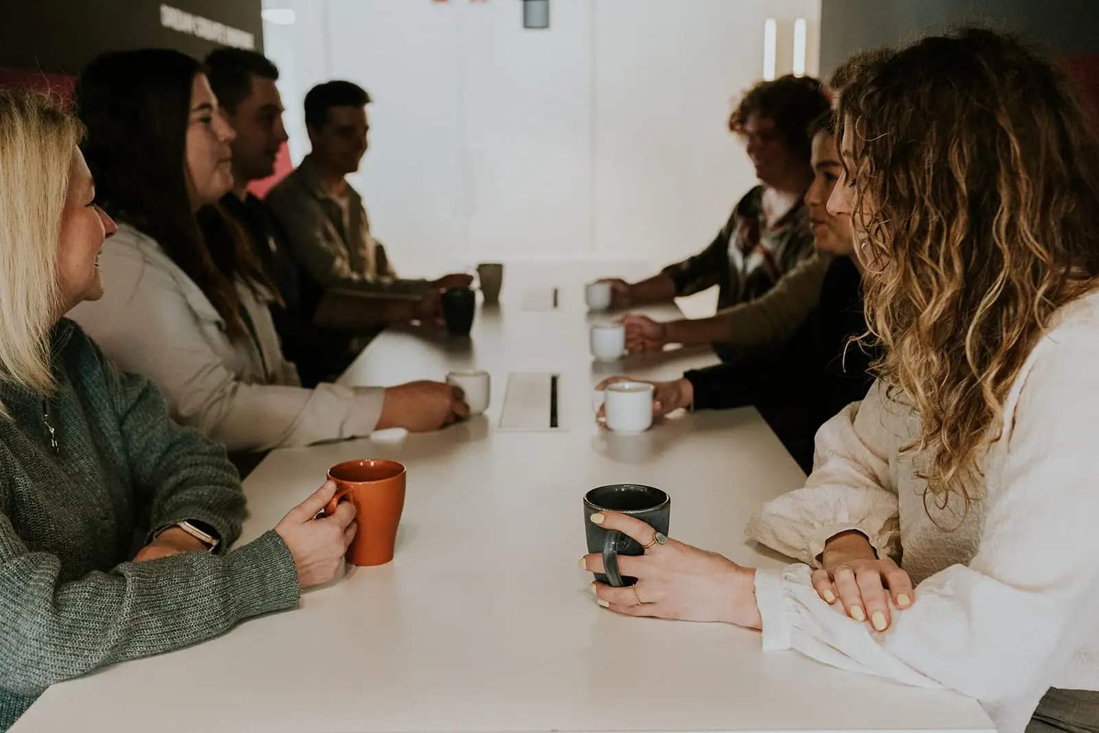 Collega’s praten met een koffie aan een lange tafel