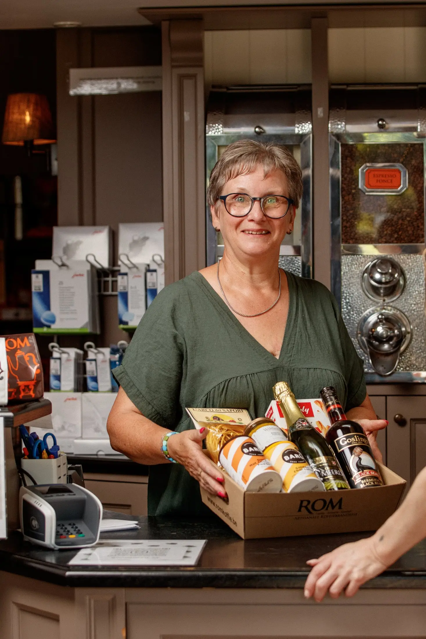 Medewerkster overhandigt lachend een ROM-doos met koffie en streekproducten aan de toonbank